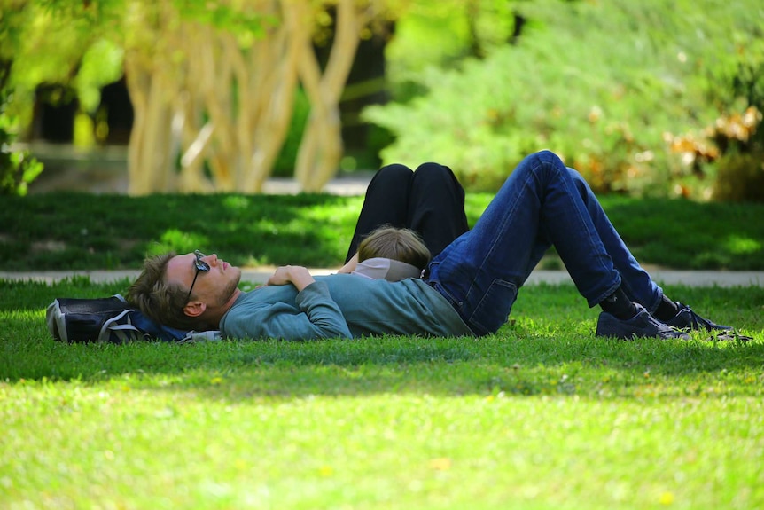 A man and a woman nap in a park.
