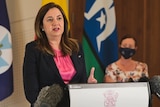 A woman with brown hair and a pink top and lipstick answers questions from the media at a lecturn.