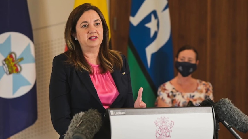 A woman with brown hair and a pink top and lipstick answers questions from the media at a lecturn.