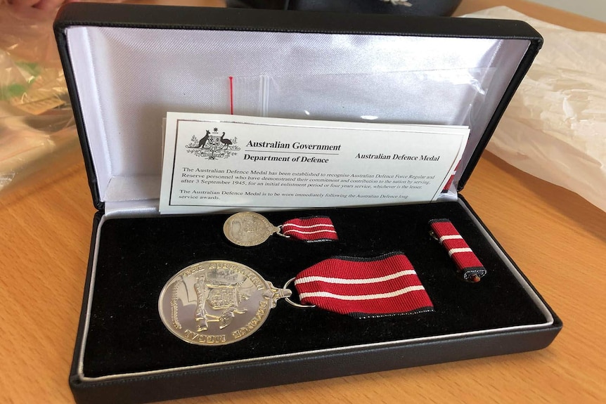 The Australian Defence Medal sits in a protective box. Its ribbon is red with white stripes.