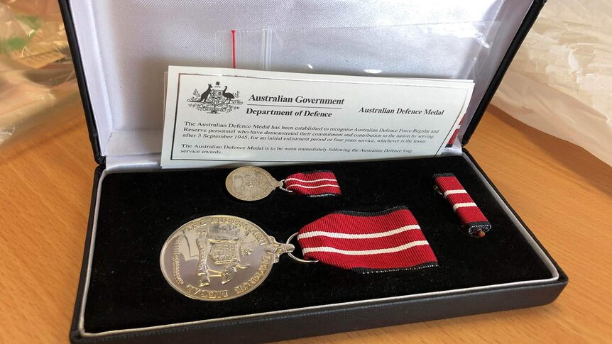 The Australian Defence Medal sits in a protective box. Its ribbon is red with white stripes.