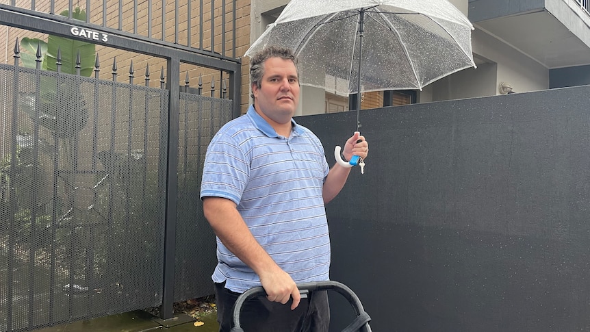 A man standing outside an apartment holding an umbrella and pram.