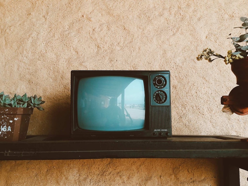 A small old television stands on a shelf.