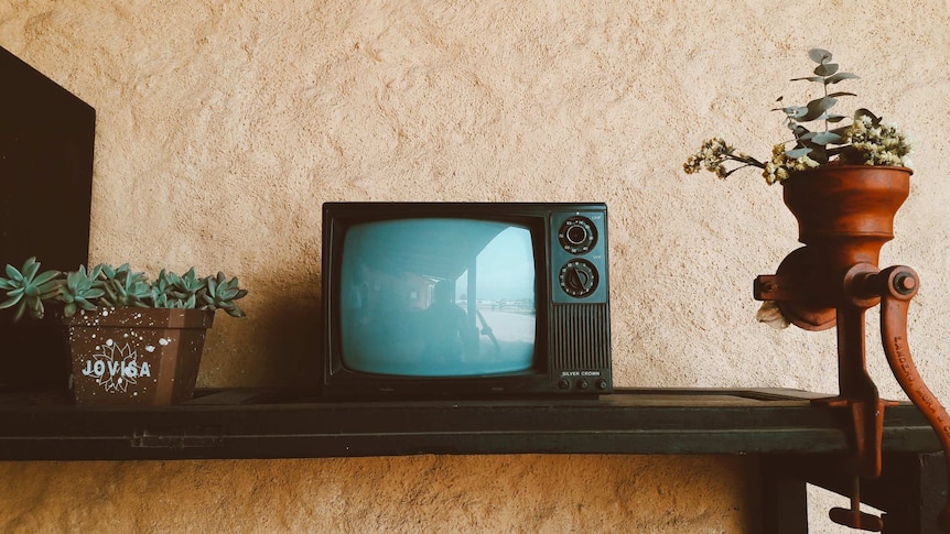 A small old television stands on a shelf.