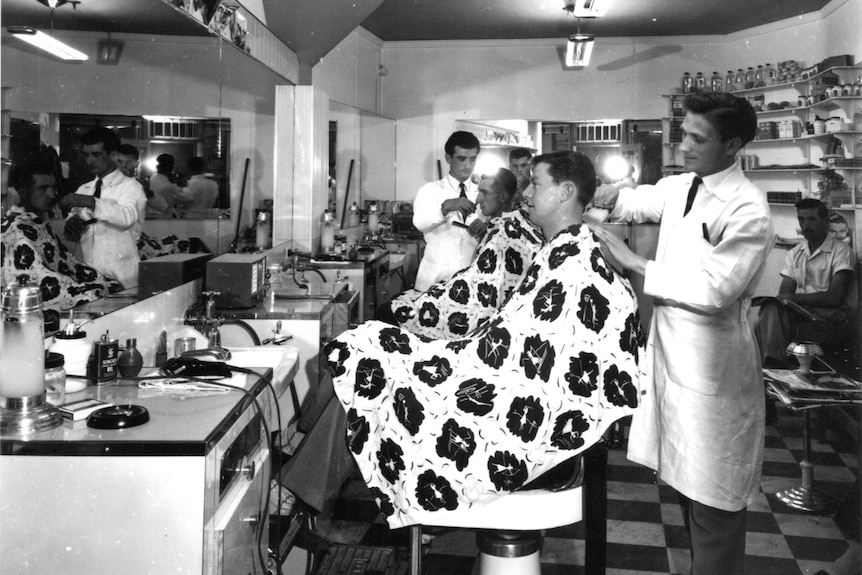 black and white image of two barbers cutting their clients' hair, in front of mirror