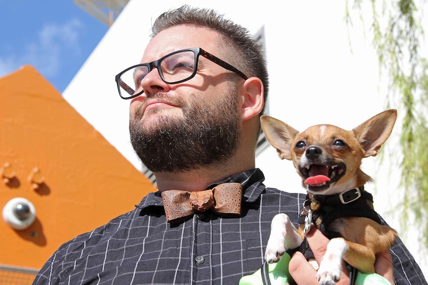 A photo of Darwin man Tom Kelly as he holds his pet chihuahua, looking into the sun.