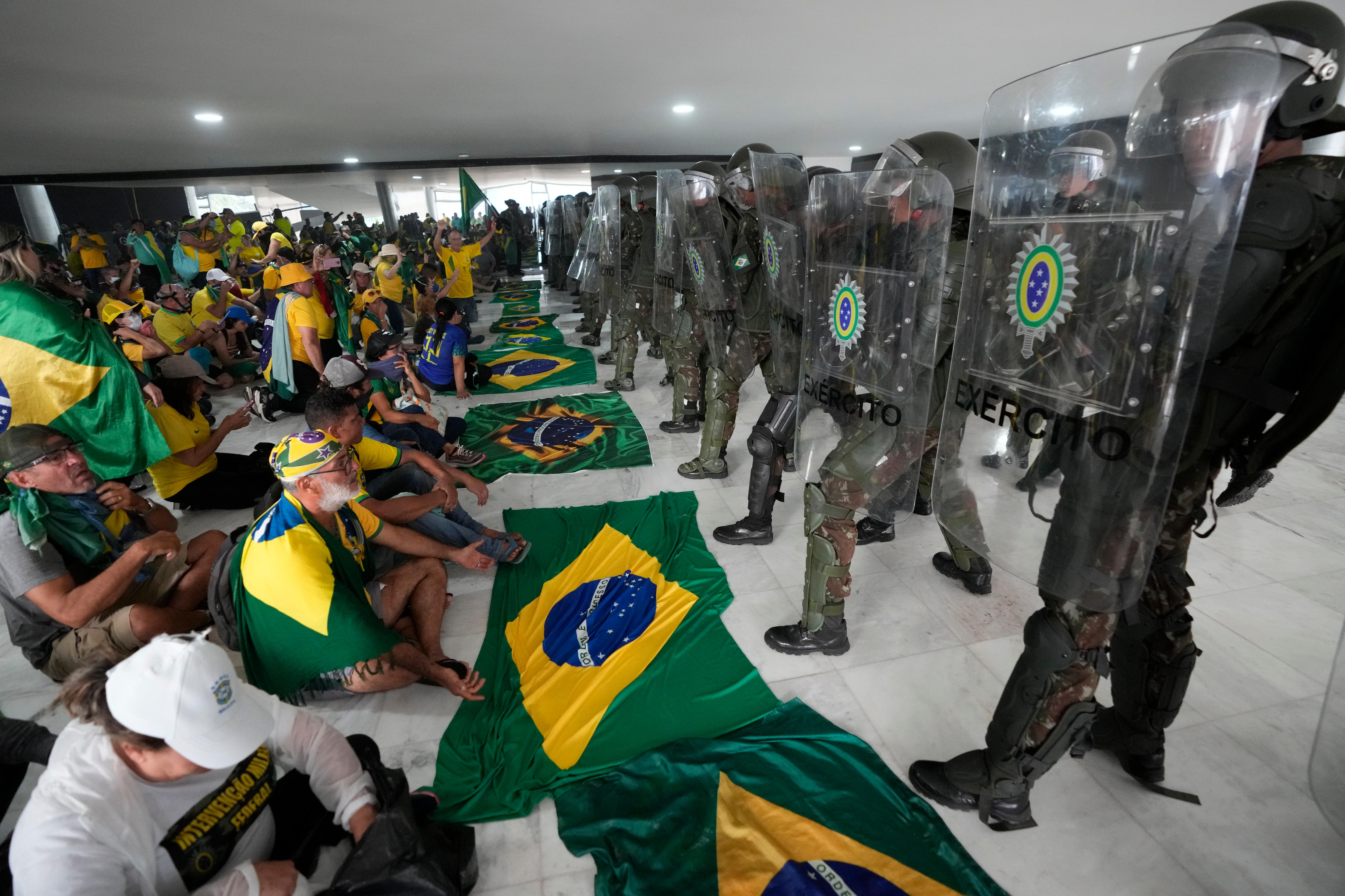 抗议者坐在地上，在防暴警察面前举着一排巴西国旗。