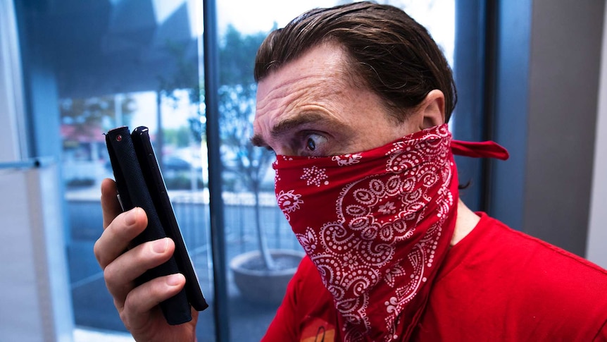 A man with a handkerchief over his mouth and nose looks fearfully at a smart phone.