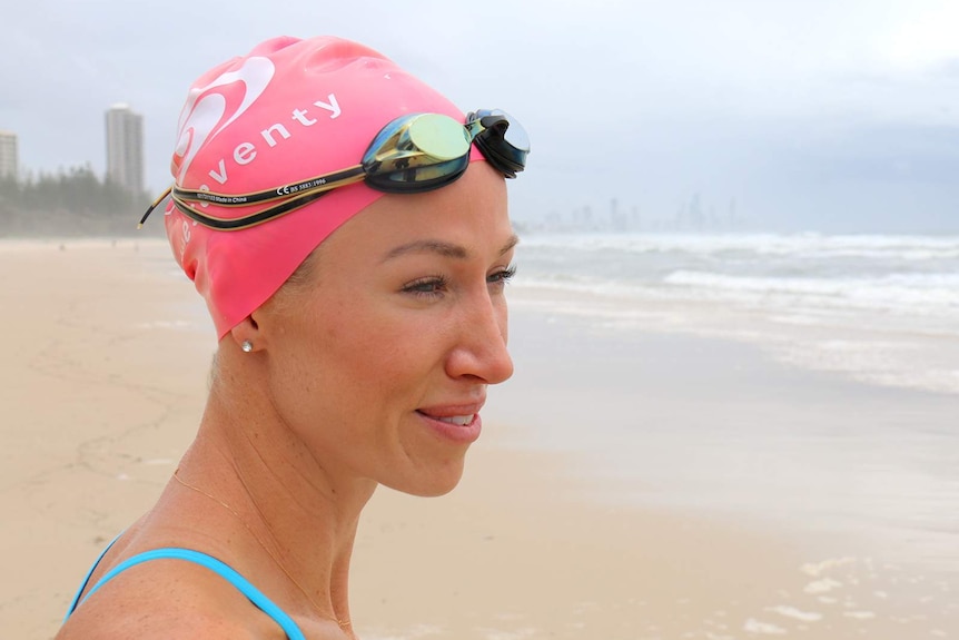 A woman in a swimming cap smiles as she stares at the ocean on a Gold Coast beach