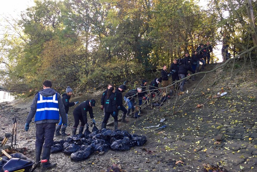 Thames 21 volunteers take bags of rubbish from the river bed.