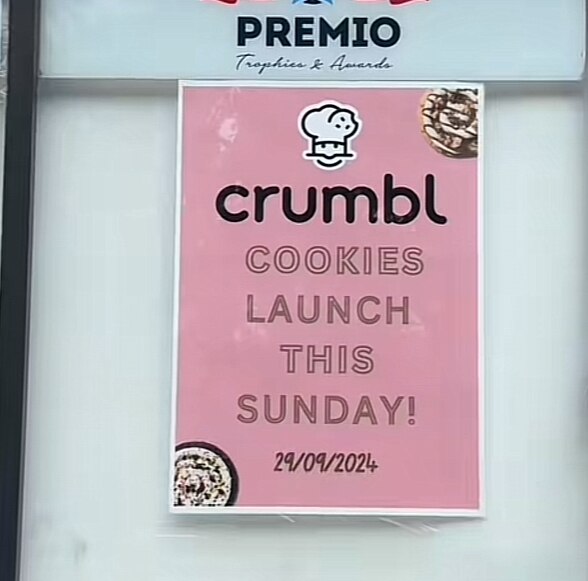 A pink sign that reads "Crumbl Cookies Launch This Sunday 29/9/2024"