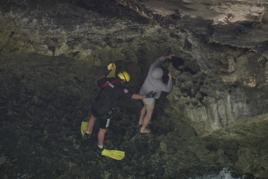 A man being held down from rocks by a rescue worker