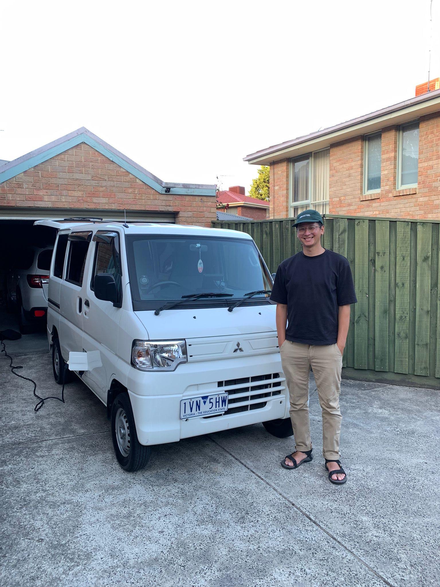 A man stands in front of his white electric caravan while charging it. 