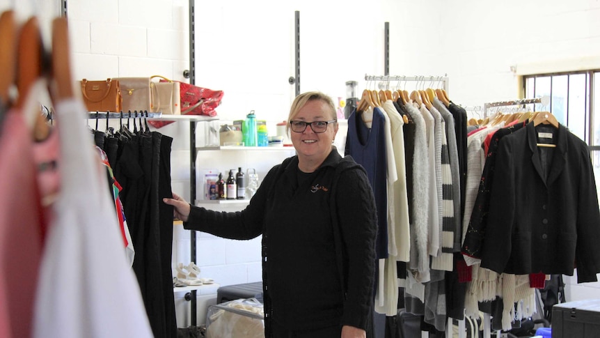 A woman standing by a clothes rack in an op shop.