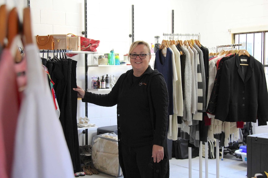 A woman standing by a clothes rack in an op shop.