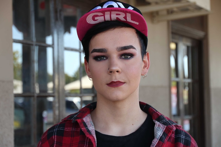 A young man wearing makeup looks at the camera