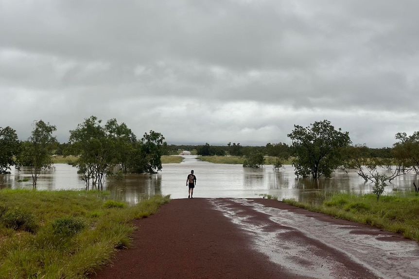 A person stands at the edge of a flooded outback road.