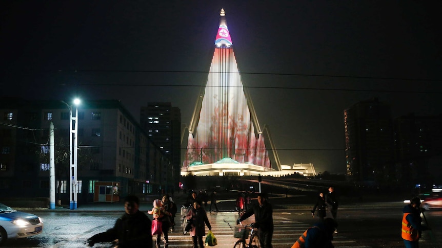 People cross a street as pyramid-shaped Ryugyong Hotel is seen in the background.