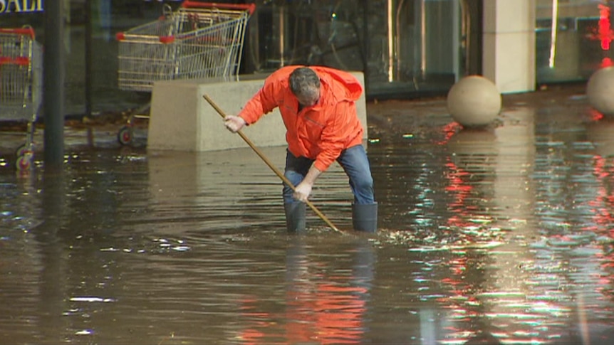 A man in an orange jacket cleaning up flood water