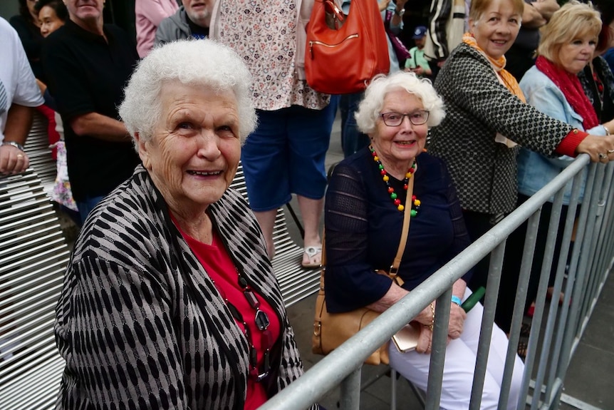 Moree Southwell and Evelyn Talbot sit in chairs with a front row seat to the parade on a rainy day in Melbourne.