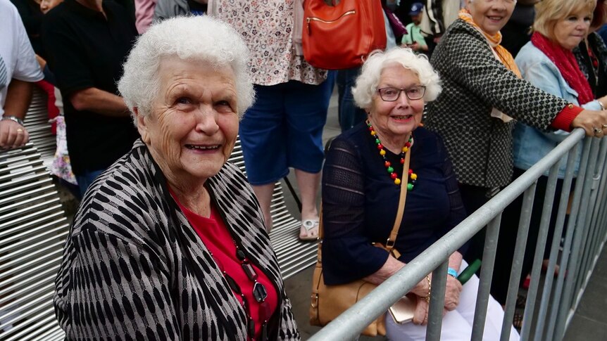 Moree Southwell and Evelyn Talbot sit in chairs with a front row seat to the parade on a rainy day in Melbourne.