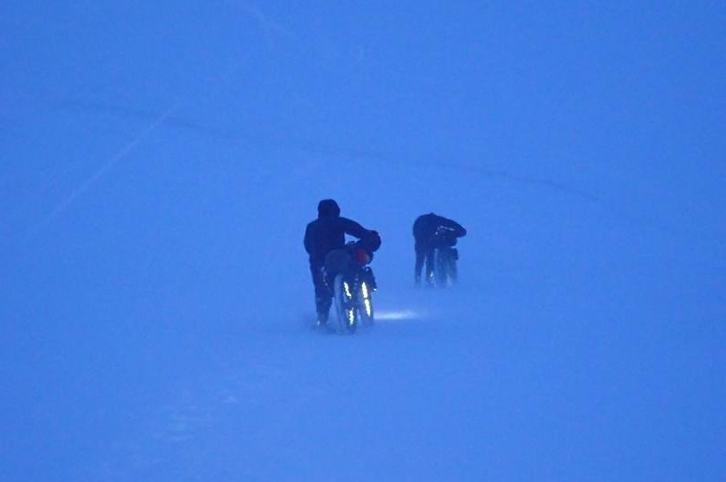 Two people pushing bicycles through a snow storm.