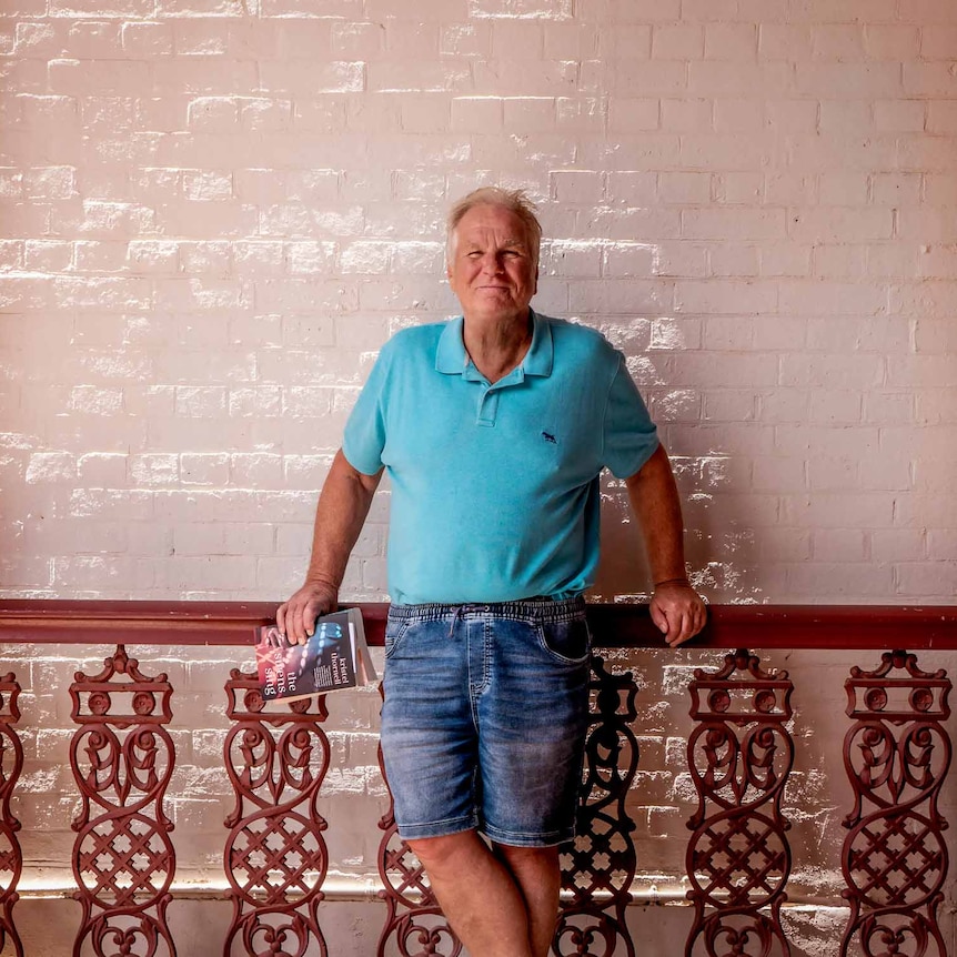 Rick Whittle, leaning against a railing with a white tile wall in the background.