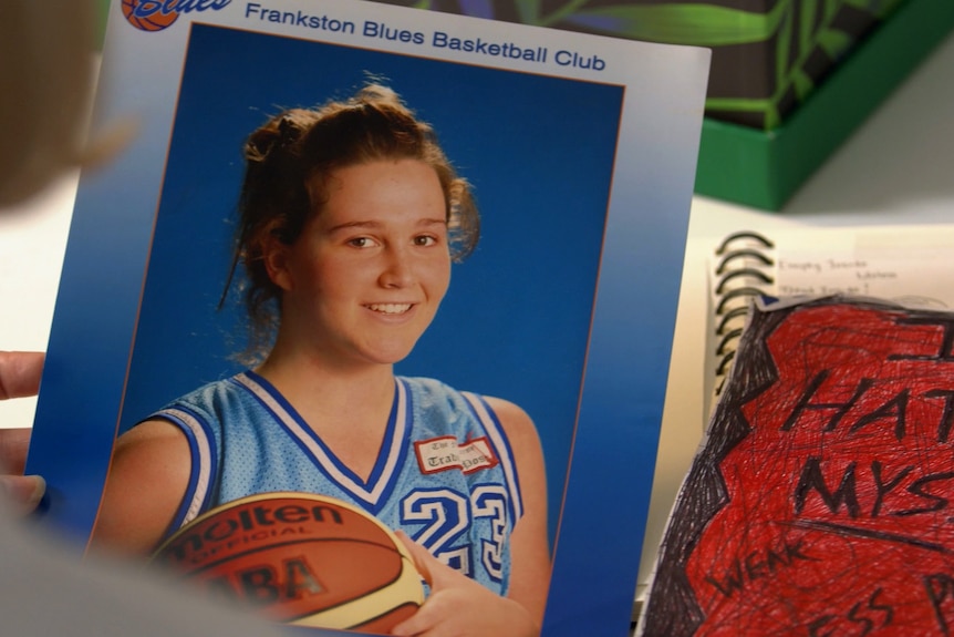 A photo of a young woman with a basketball being held near a notebook with 'I hate myself' scrawled in large angry letters.