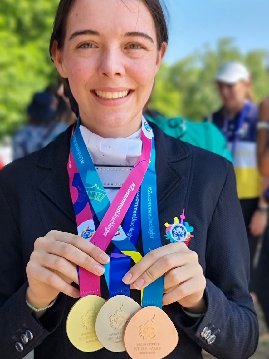 A smiling young woman with dark hair displaying her Special Olympics medals.