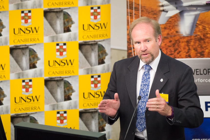 Man at lecture with University of New South Wales logos in the background