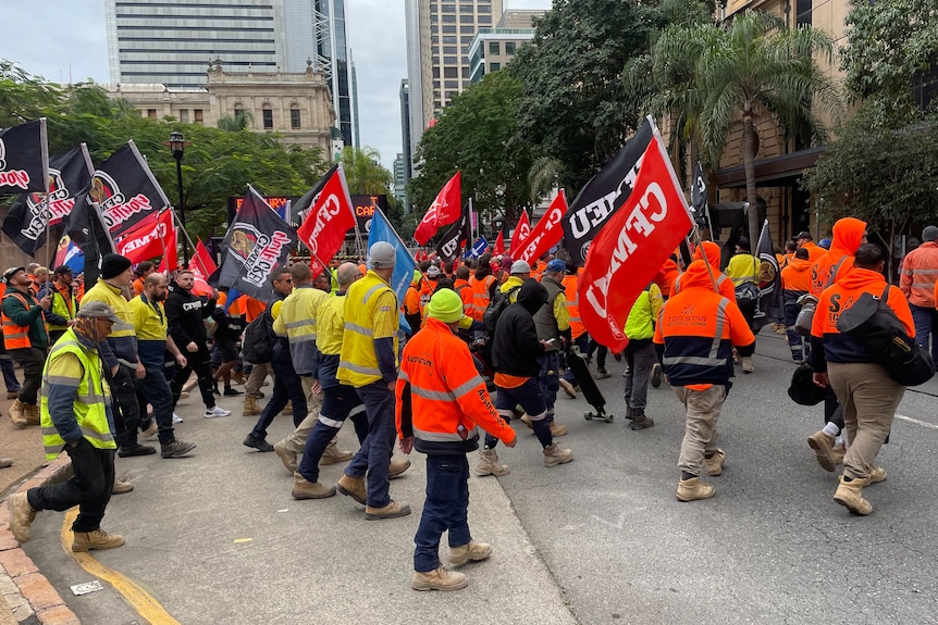 Workers in construction uniforms hold CFMEU flags as they march in protest