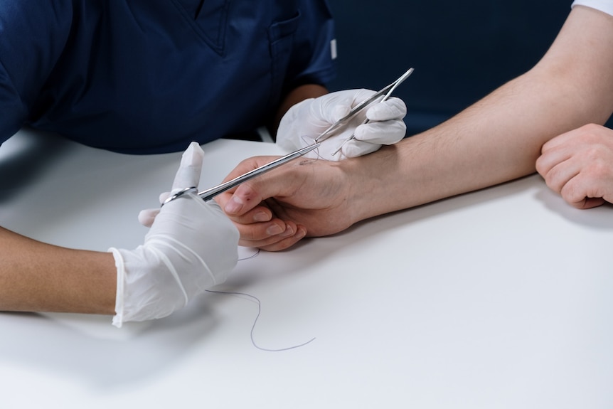 A doctor uses stitches to close up a wound on a patient's wrist