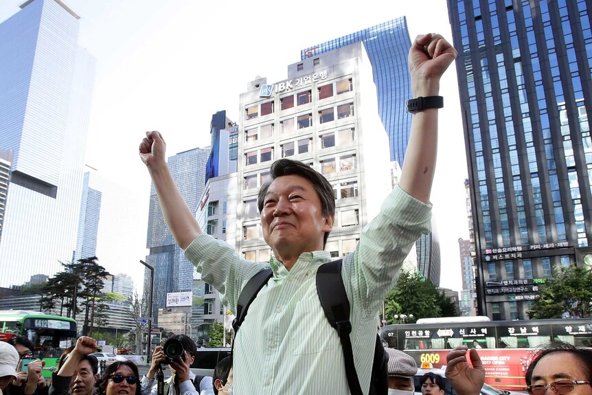 South Korean presidential candidate Ahn Cheol-Soo stands in an urban square with two fists raised above his head in victory.