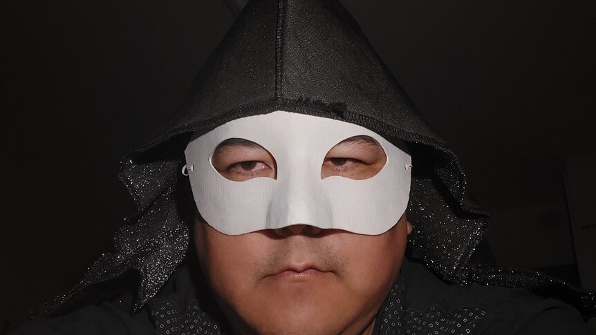 Vegan poet Marcus Ten Low wears a black hood and white masquerade mask.