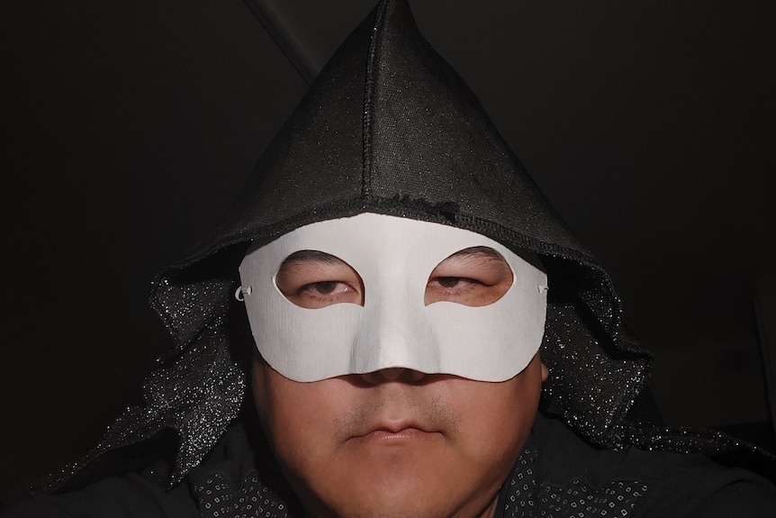 Vegan poet Marcus Ten Low wears a black hood and white masquerade mask.