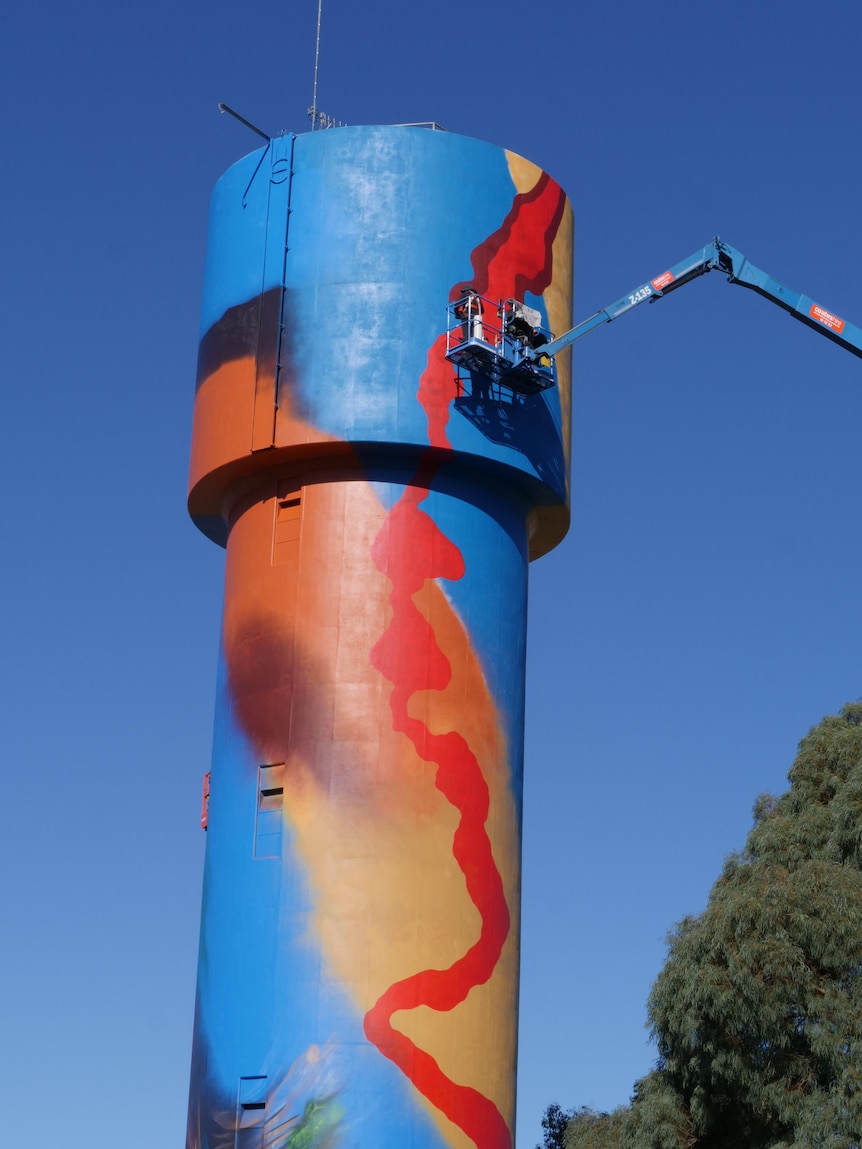 A colourful water tower with artists painting aboriginal imagery of a lava flowing down it