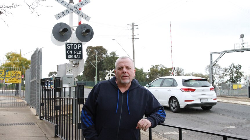 A man stands in front of a railway level crossing