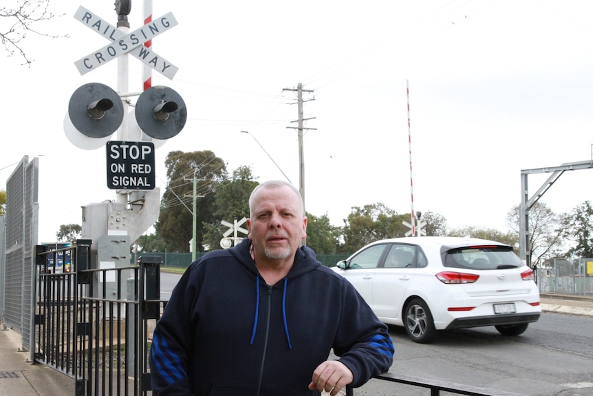 A man stands in front of a railway level crossing