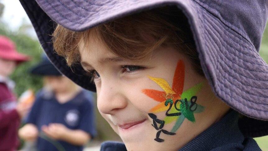 A close up of a child with their face painted with the multi-coloured 2018 Commonwealth Games logo