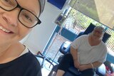 Two women in a hospital ward wearing bandanas smile for a selfie.