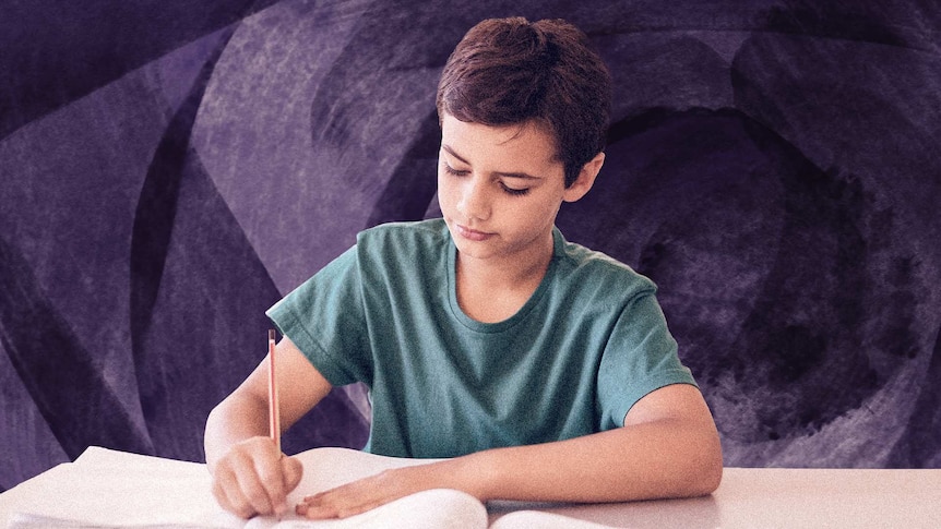 A boy sits at a desk writing on paper with a pencil.
