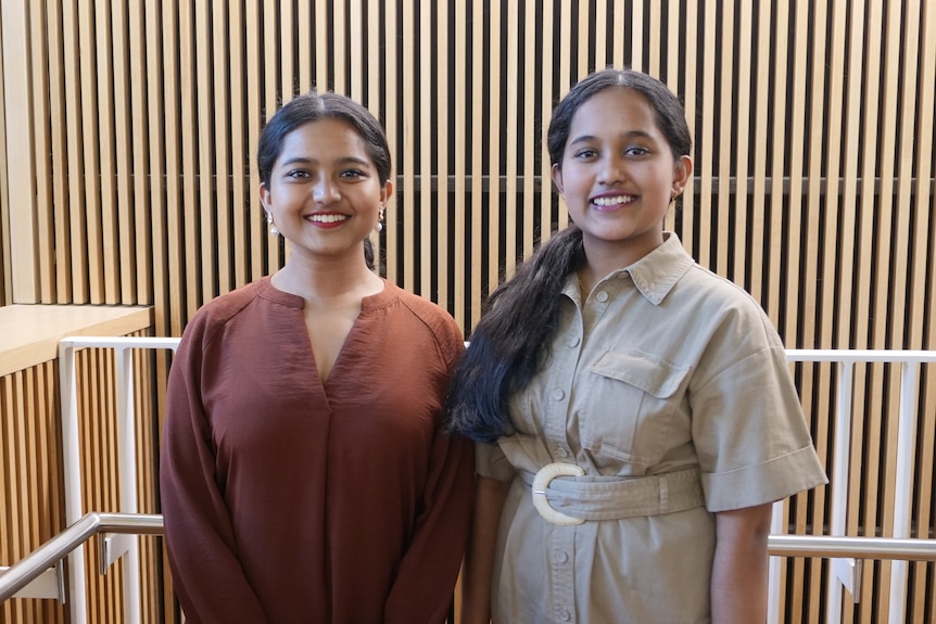 Two young women stand in a stairwell, smiling.