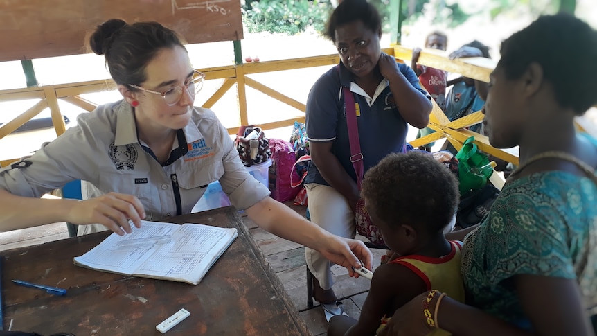 Caucasian female doctor treating a PNG mother and child. 