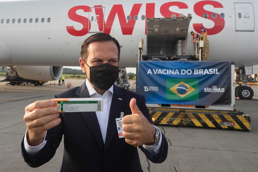 A man holding a box of COVID-19 vaccine at an airport in Brazil.