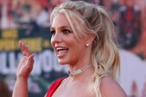 Britney Spears waves off camera with her mouth open wearing a red dress at a movie premiere
