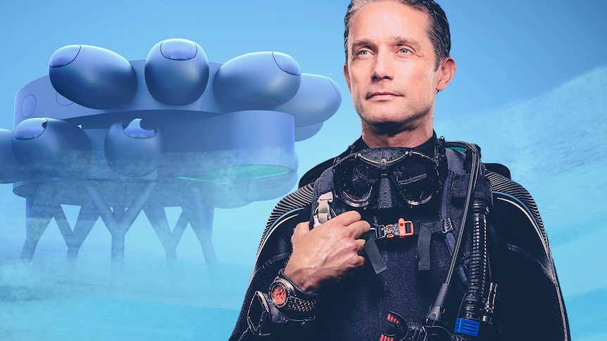 Fabien Cousteau in scuba equipment stands in front of a conceptual rendering of an underwater research station.