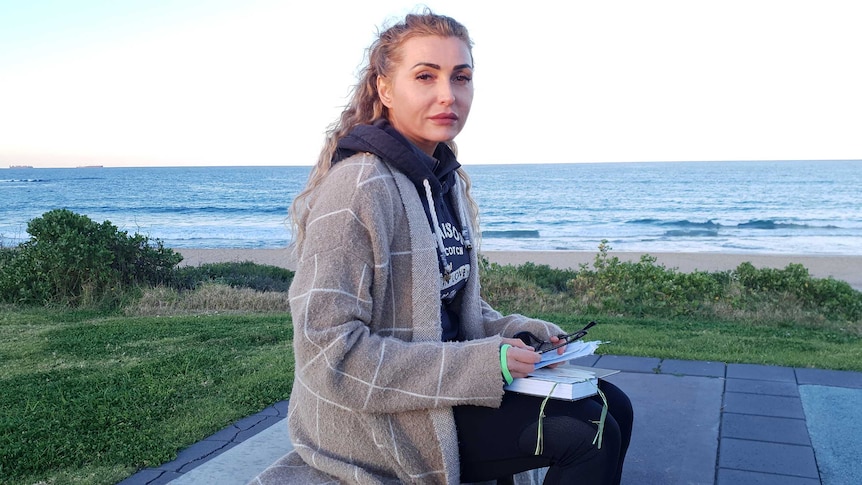 A woman sits down next to a beach.