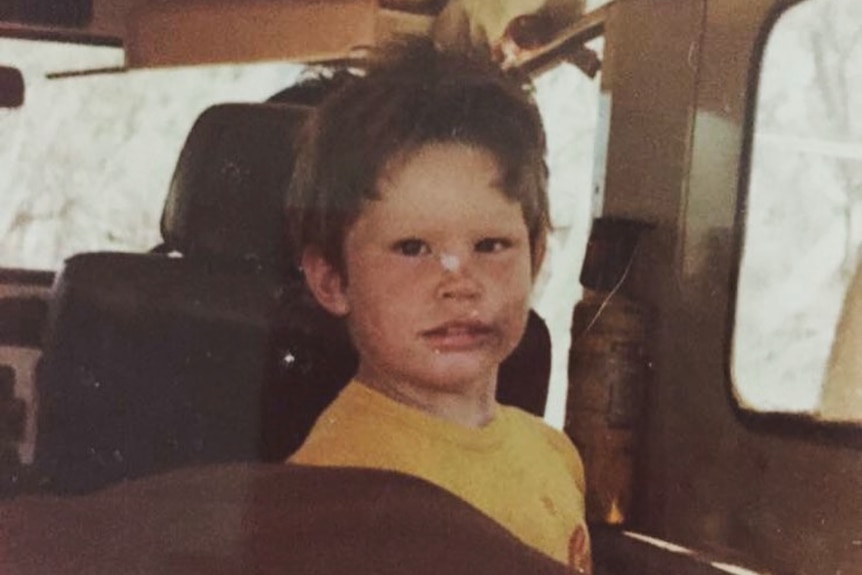 An old photo of a child sitting in the back seat of a car.