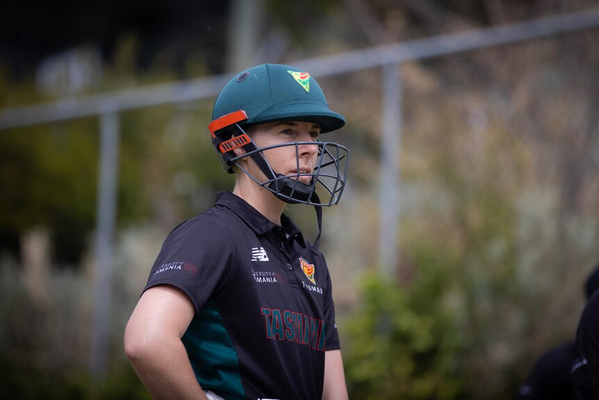 A woman wearing a cricket helmet looks into the distance.