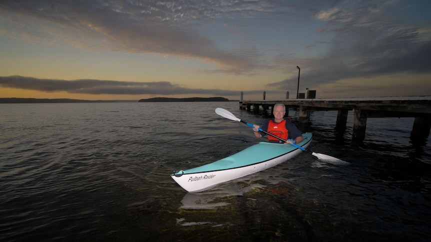 Scott Bevan kayaking by a pier; it's just before dawn.